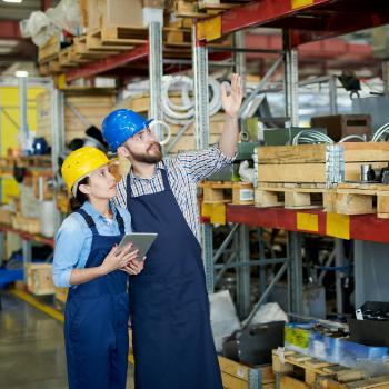 two employees carry out code enforcement in warehouse with wood planks
